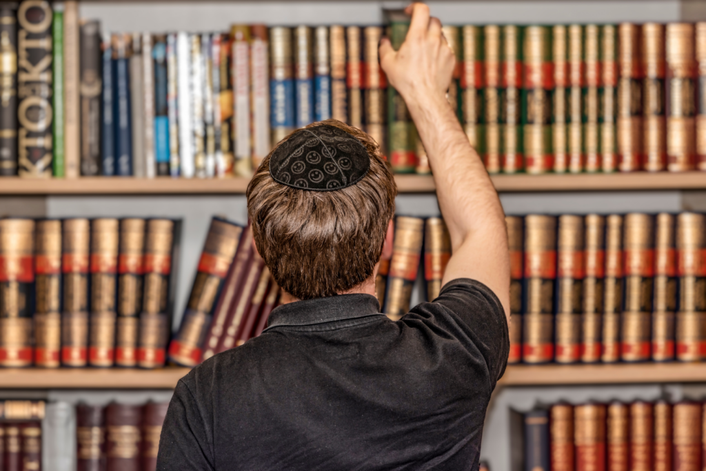 Person from behind wearing kippah reaching for book in library